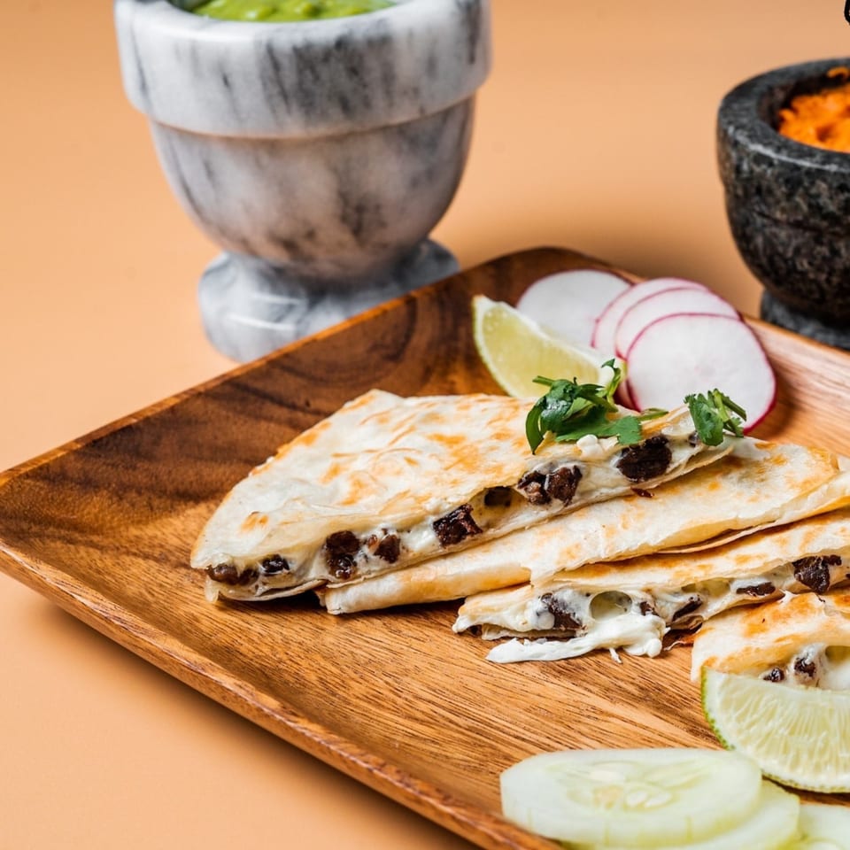 La Familia quesadillas with melted cheese and meat, garnished with lime, radish, and cilantro.