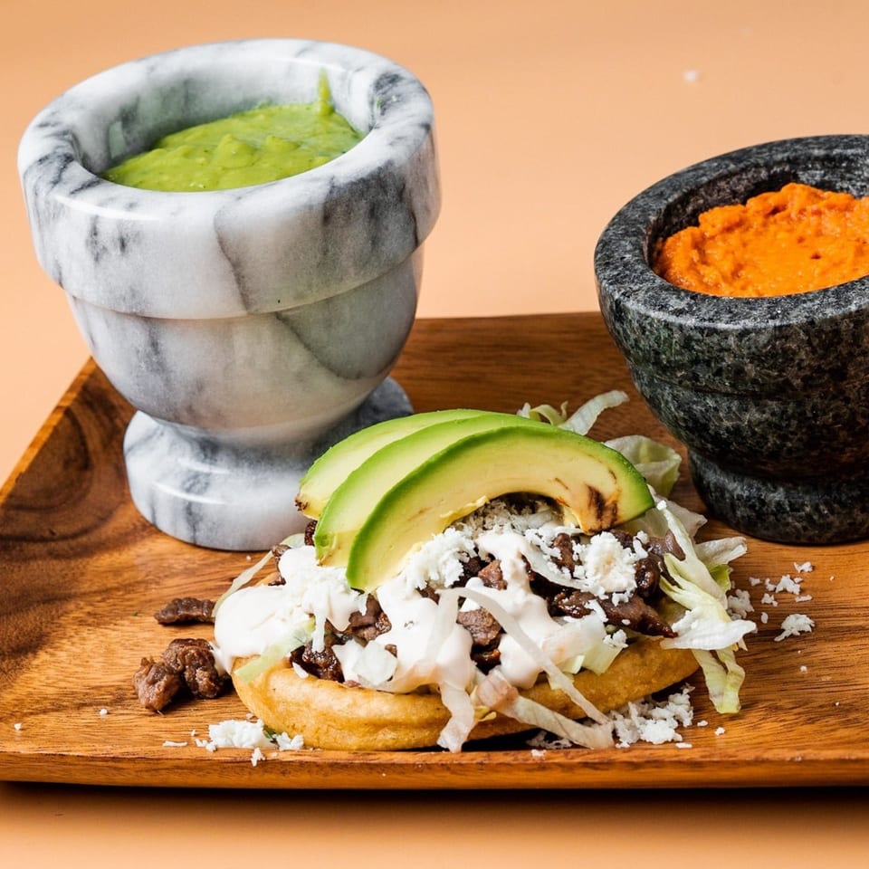 La Familia Mexican sopes with meat, cheese, lettuce, avocado, and two bowls of salsa.