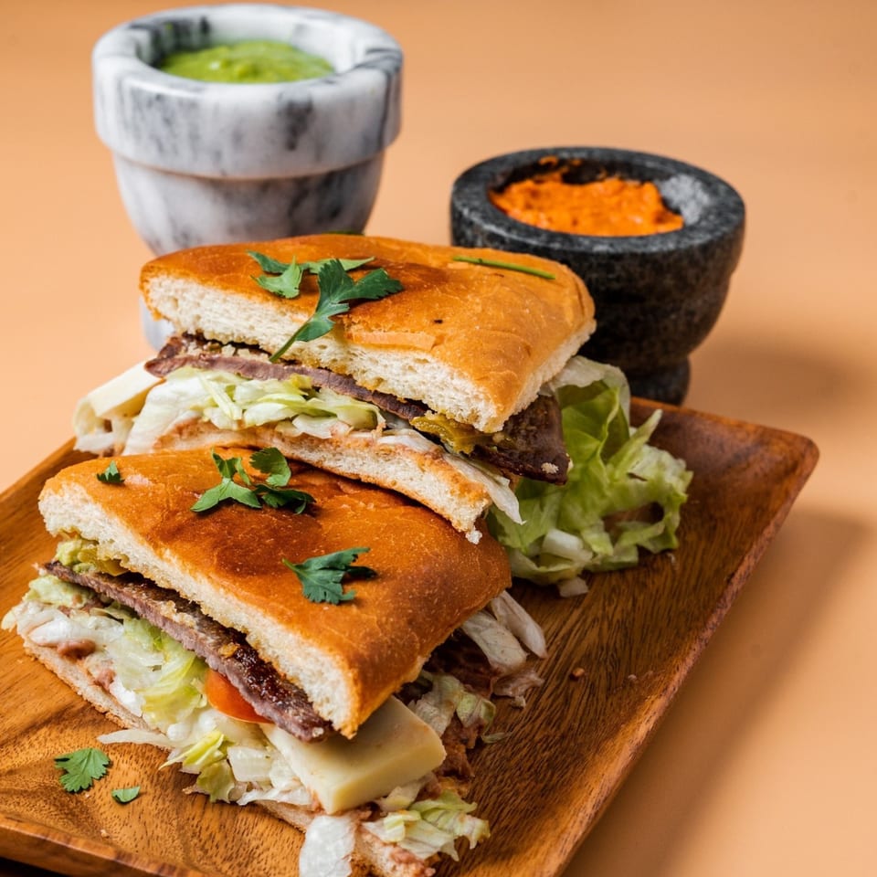 Two La Familia Mexican tortas with meat, cheese, and lettuce, served with guacamole and salsa.