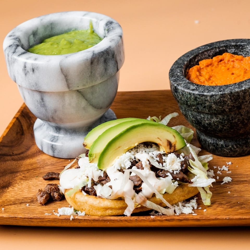 La Familia sopes with meat, avocado, cheese, and lettuce, served with green and red salsas.